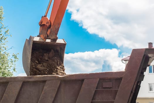 Excavation works. The bucket of the tractor loads the soil with a shovel into the back of a dump truck on the construction site.