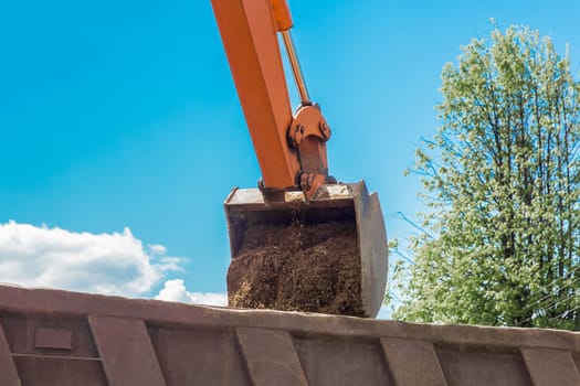 Excavation works. The bucket of the tractor loads the soil with a shovel into the back of a dump truck on the construction site.