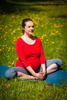Pregnancy yoga exercise - pregnant woman doing asana baddha konasana bound angle pose outdoors on grass lawn with dandelions in summer