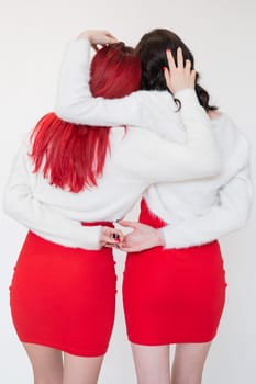 Rear view of two women dressed in identical red dresses and white sweaters. Lesbian intimacy. White background