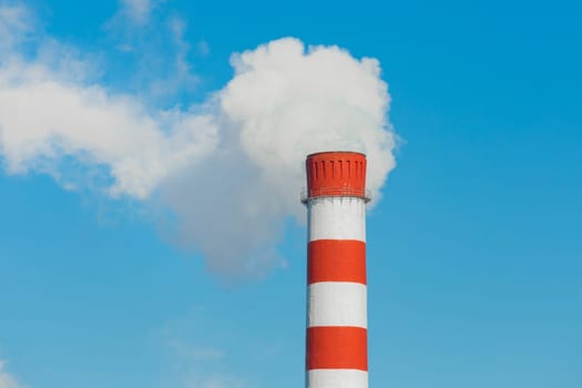 Pollution of the environment, ecology and air. Withdrawal of combustion products of soot, smoke and gases from the pipe of an industrial plant into the atmosphere against the background of a blue sky.