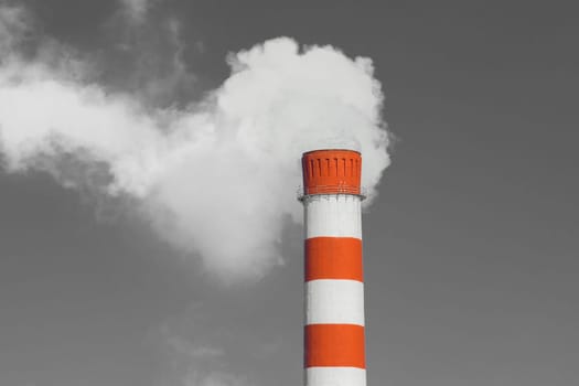 Pollution of the environment, ecology and air. Withdrawal of combustion products of soot, smoke and gases from the pipe of an industrial plant into the atmosphere against the background of a gray sky.