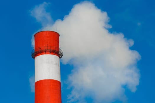 Pollution of the environment, ecology and air. Withdrawal of combustion products of soot, smoke and gases from the pipe of an industrial plant into the atmosphere against the background of a blue sky.