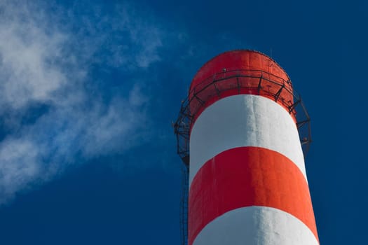 Pollution of the environment, ecology and air. Withdrawal of combustion products of soot, smoke and gases from the pipe of an industrial plant into the atmosphere against the background of a blue sky.