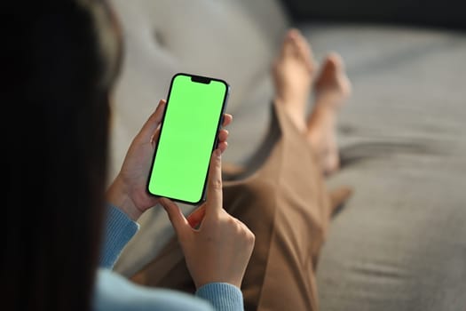 Young woman home use green screen mockup Smartphone, her sitting on sofa in living room. High quality photo