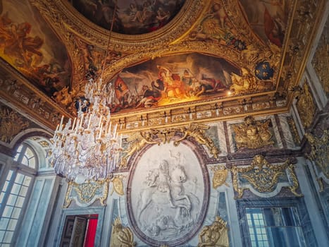The War Room, Palace of Versailles, France. Chandelier hangs out of the golden painted ceiling and the stucco medallion of Louis XIV on horseback