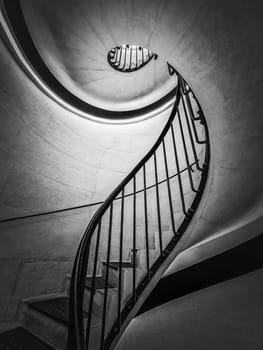 Black and white abstract view of a stairwell with metal handrail. Spiral stairway, hypnotic form