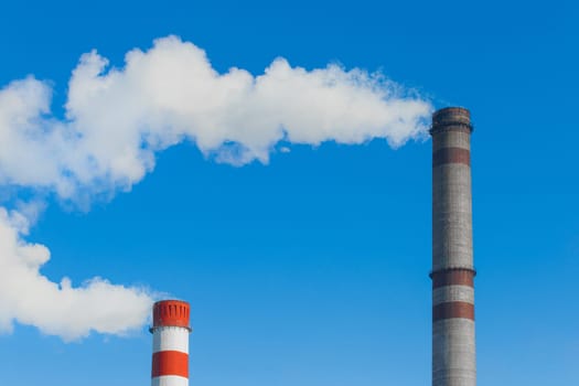 Pollution of the environment, ecology and air. Withdrawal of combustion products of soot, smoke and gases from the pipe of an industrial plant into the atmosphere against the background of a blue sky.