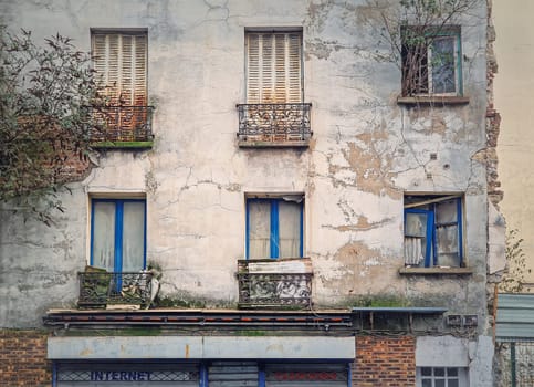 Abandoned building facade. Trees and bushes growing out of windows, rusted louvers and cracked concrete walls