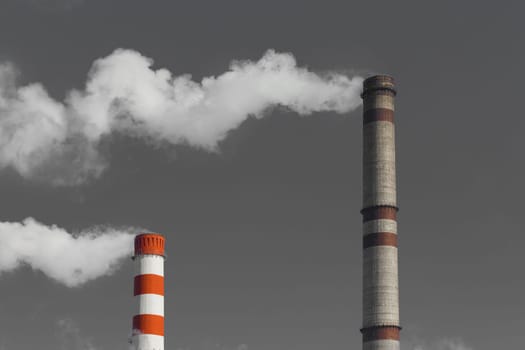 Pollution of the environment, ecology and air. Withdrawal of combustion products of soot, smoke and gases from the pipe of an industrial plant into the atmosphere against the background of a gray sky.