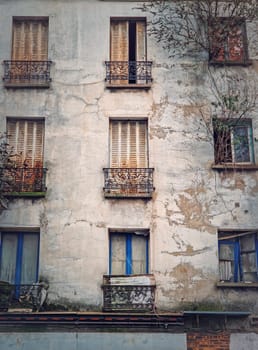 Abandoned building facade. Trees and bushes growing out of windows, rusted louvers and cracked concrete walls