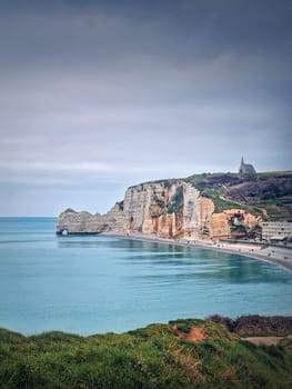 Idyllic view to Etretat coastline with the famous Notre-Dame de la Garde chapel on the Amont cliff. Shore washed by Atlantic ocean waters, Normandy, France