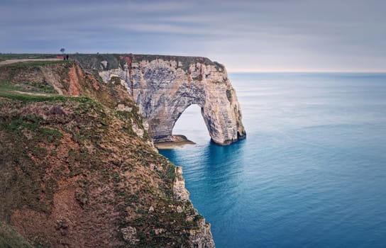 Sightseeing view to the Porte d'Aval natural arch cliff washed by Atlantic ocean waters at Etretat, Normandy, France. Beautiful coastline scenery with famous Falaise d'Aval