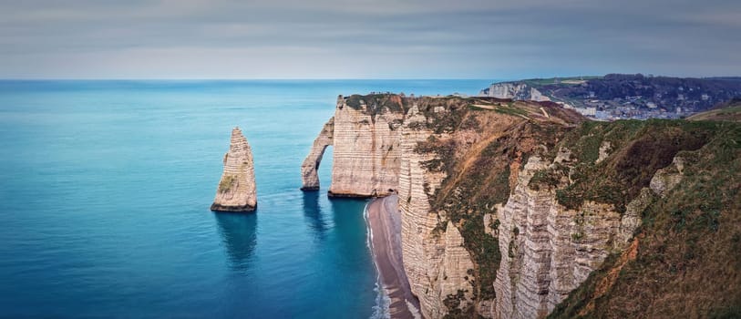Panoramic view to the famous rock Aiguille of Etretat in Normandy, France. Limestone cliffs Falaise d'Aval washed by La Manche channel waters. Beautiful coastline panorama