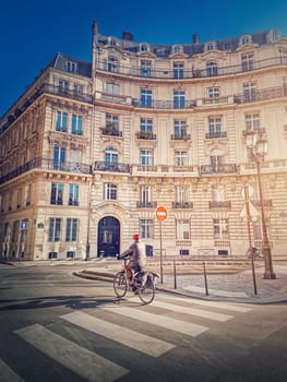 Lone man riding a bicycle near a crosswalk on the Paris city street in the morning, France