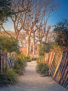 Narrow footpath in the park along wooden fence, plants and sycamore trees in the square of Asnieres-sur-Seine mairie, Paris, France