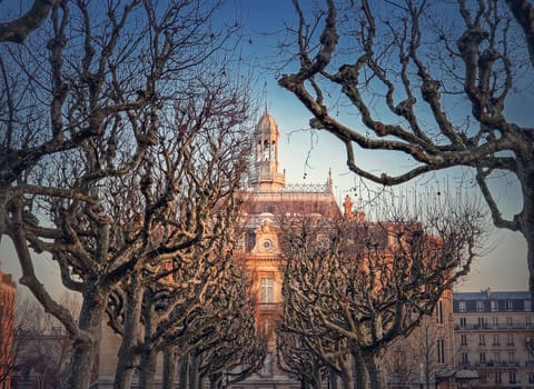 City Hall of Asnieres as seen through the leafless sycamore trees alley outdoors in the park. Asnières-sur-Seine mairie backyard facade view in sunset light, northwestern suburb of Paris, France