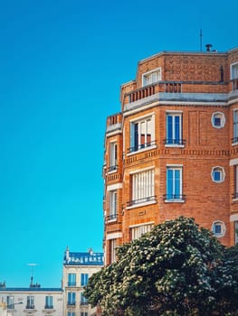 Beautiful orange brick building with a blooming tree at the bottom under a clear blue sky background in Asnieres-sur-seine a suburb of Paris, France