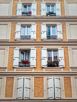 Building facade with yellow painted walls of brick masonry and windows with white outdoors louvers