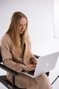 A business woman in a suit is working, typing on a laptop apple and sitting on a producer chair. portrait blonde assistant of hands with computer MacBook . Vertical