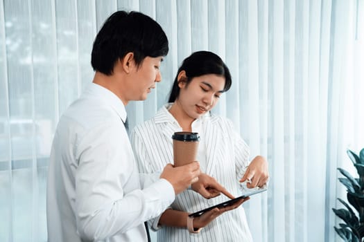 Manager advising guiding younger colleague with tablet in workplace. Couple businesspeople in formal wear working together on financial strategy as concept of teamwork and harmony in office.