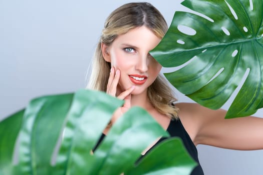 Closeup woman with perfect clean skin and alluring flawless natural soft facial makeup holding green leave monstera. Natural skincare treatment beauty or spa concept in isolated background.