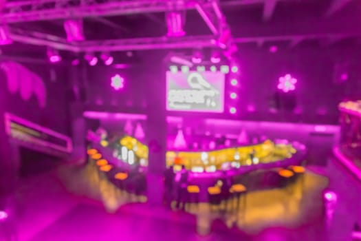 Blurred modern abstract interior of a nightclub with neon purple lighting on the walls.