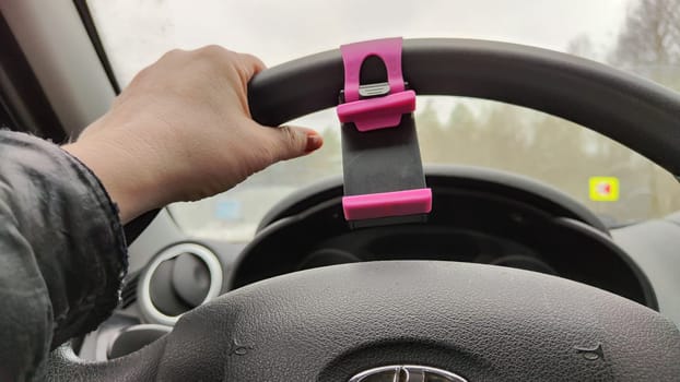 Hand of woman on the steering wheel in a car and forest and snow on the side of the road on a winter day. Woman driving car in winter travel in landscape with snow covered woods