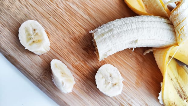 Banana with open panel and sliced round pieces on wooden board and white background. Ripe banana with peel cooking, Close up. Delicious sweet fruit dessert