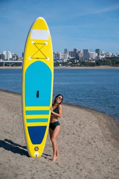 Caucasian woman walks along the beach and carries a sup board on the river in the city. Summer sport