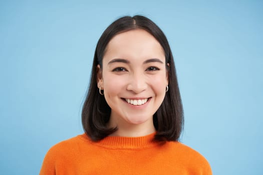 Close up portrait of beautiful korean woman with healthy smile, natural clear facial skin, stands over blue background.