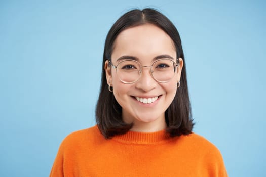 Portrait of smiling beautiful woman in glasses, testing her eyesight, wearing new spectacles, standing over blue background.