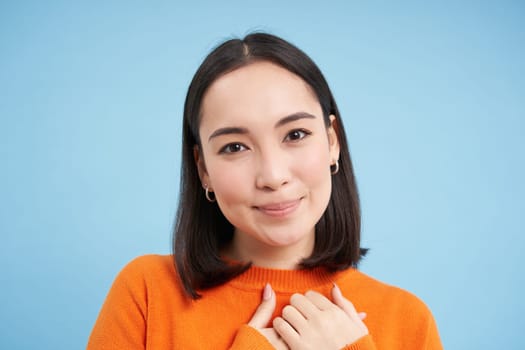 Close up portrait of beautiful korean woman with healthy smile, natural clear facial skin, stands over blue background.