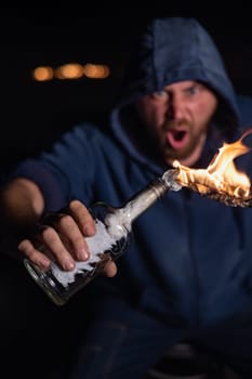 The man in the hood is holding a burning bottle. Molotov cocktail