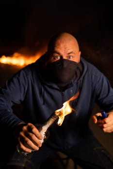 A masked man is holding a burning bottle. Molotov cocktail