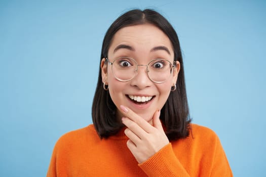 Portrait of smiling beautiful woman in glasses, testing her eyesight, wearing new spectacles, standing over blue background.