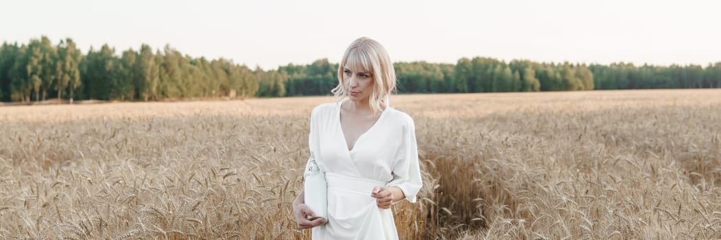A blonde woman in a long white dress walks in a wheat field. The concept of a wedding and walking in nature