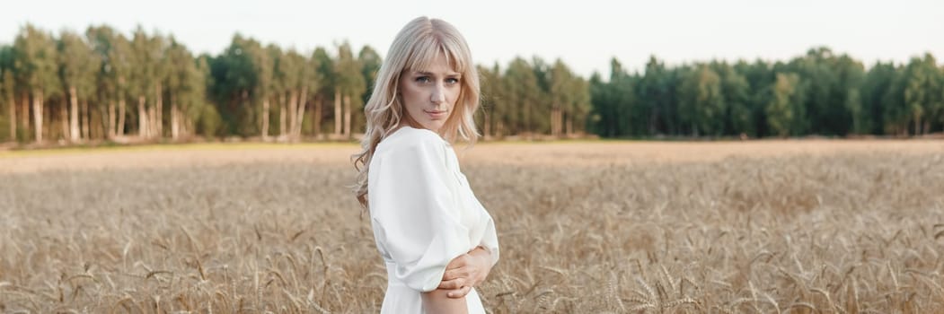 A blonde woman in a long white dress walks in a wheat field. The concept of a wedding and walking in nature