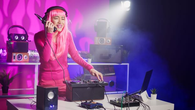 Asian performer playing electronic sound using mixer console, creating unique remix for fans during techno party in nightclub. Musician enjoying performing music using professional audio equipment