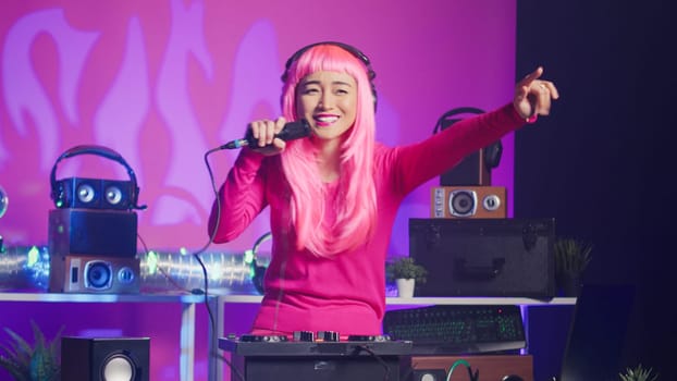 Musician standing at dj table performing electronic song using professional turntables, enjoying playing music during night time in club. Artist with pink hair doing performance with audio equipment