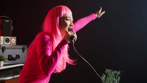 Asian dj having fun mixing eletronic music with techno using professional turntables, standing at dj table in club at night. Musical performer with pink hair and blouse enjoying performing song remix