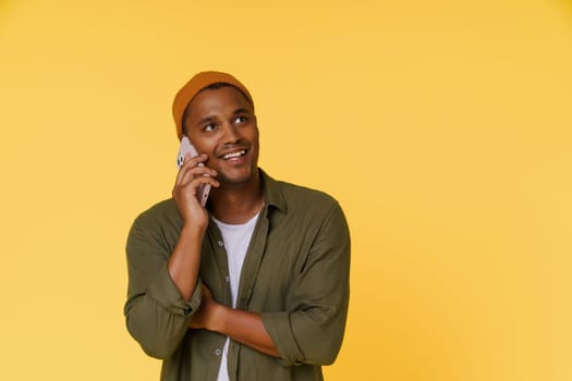 Smiling African man wearing orange cap is having phone call, with copy space on yellow background. Perfect for product placement and advertising concepts. High quality photo