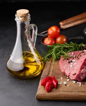 Raw piece of beef with spices pepper, rosemary sprig, salt and olive oil on a wooden board, black background