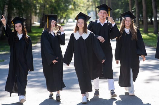 Row of happy young people in graduation gowns outdoors. Students are walking in the park