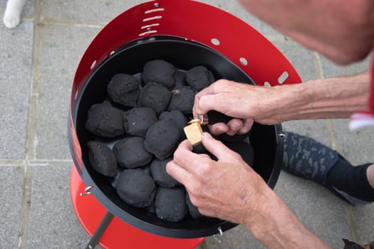 a man lights a fire with a lighter special charcoals for a barbecue a barbecue house on the terrace prepares a place for a barbecue. High quality photo