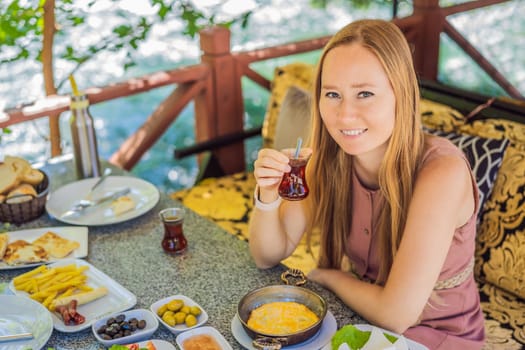 woman tourist eat Turkish breakfast. Turkish breakfast table. Pastries. Vegetables. Olives. Cheeses, fried eggs. Jams, tea in copper pot and tulip glasses. Wide composition.