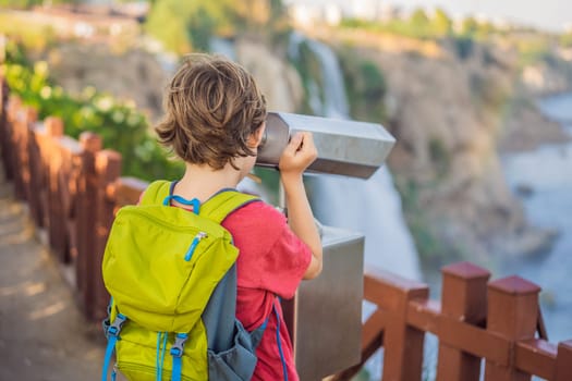 Boy tourist with a backpack on the background of Duden waterfall in Antalya. Famous places of Turkey. Lower Duden Falls drop off a rocky cliff falling from about 40 m into the Mediterranean Sea in amazing water clouds. Tourism and travel destination photo in Antalya, Turkey. Turkiye.