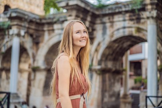 Happy female tourist traveler discover interesting places and popular attractions and walks in the old city of Antalya. Hadrian Kapisi turkey landmark city history. Popular tourist attraction - ancient Roman Hadrian Gate in old town Antalya, Turkey on a summer day. Turkiye.