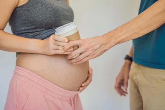 Husband forbids pregnant wife to drink coffee. A pregnant woman holds a cup of coffee in her hands. Caffeine safety, myths about coffee during pregnancy concept.