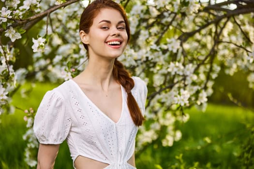 a joyful, carefree woman in a light dress stands against the background of a flowering tree. High quality photo